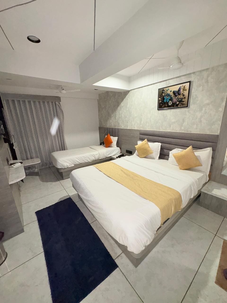 Une chambre d’hôtel moderne équipée d’un grand lit, d’un lit plus petit, d’un bureau et d’un ventilateur de plafond.