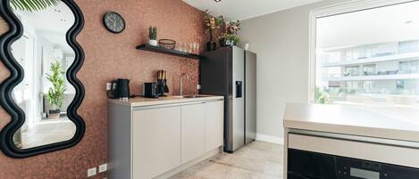 A modern kitchen with a stone backsplash, a black wavy mirror, a clock, and a refrigerator.