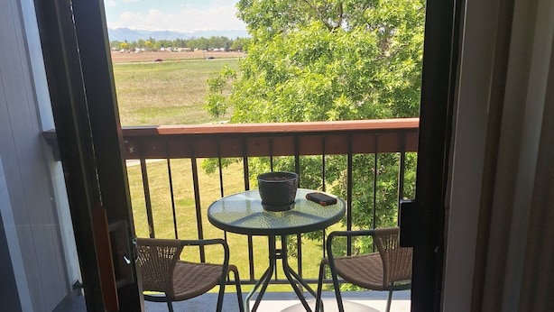 En balkon med et rundt bord, to fletstole, en potteplante og en smartphone på bordet.