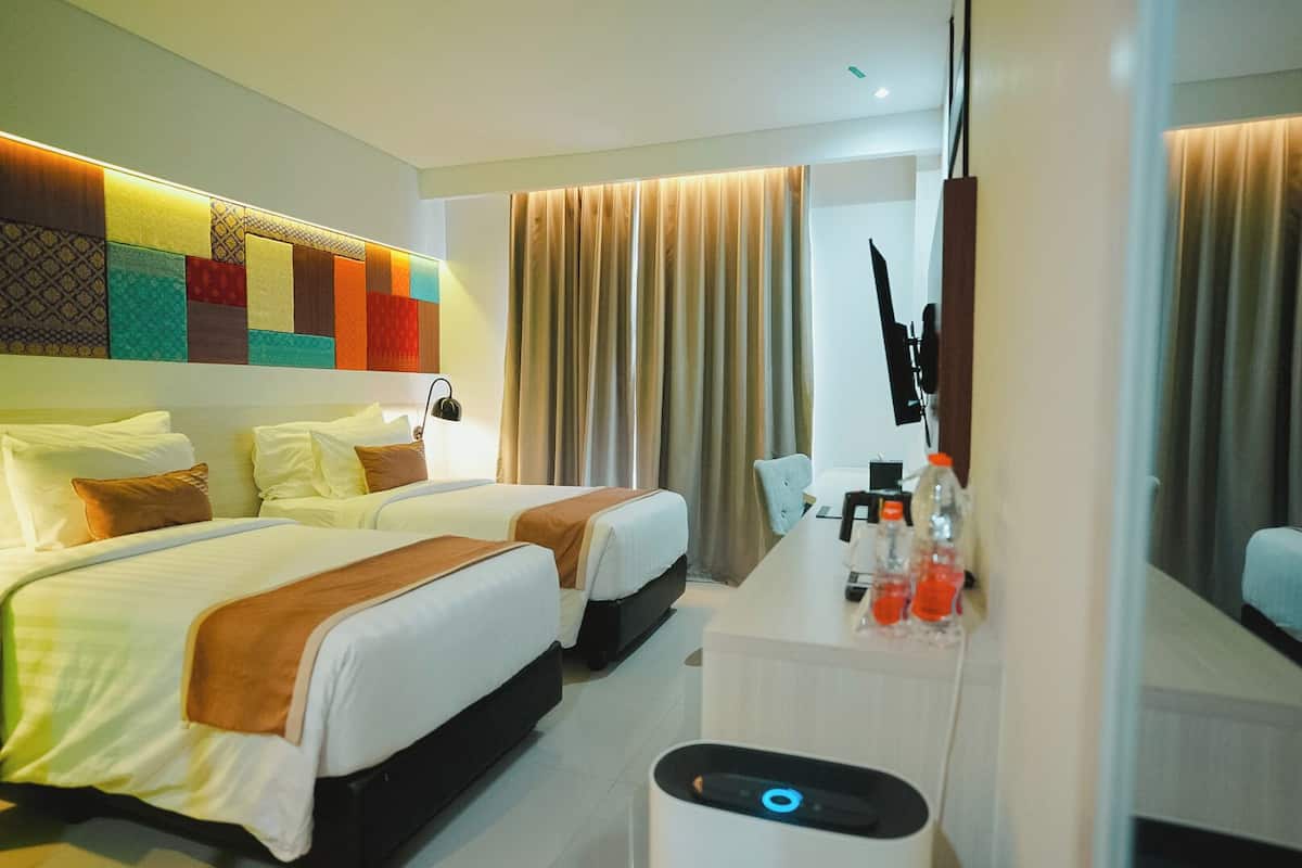 Ein Hotelzimmer mit zwei Betten, einem Schreibtisch mit Pflegeartikeln, einem Spiegel und einem großen Fenster mit Vorhängen.