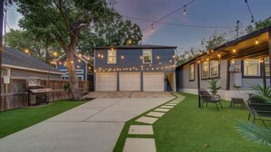 Ein Garten mit Kunstgrasanlage, einer Betonterrasse, einem Grill und Lichterketten.