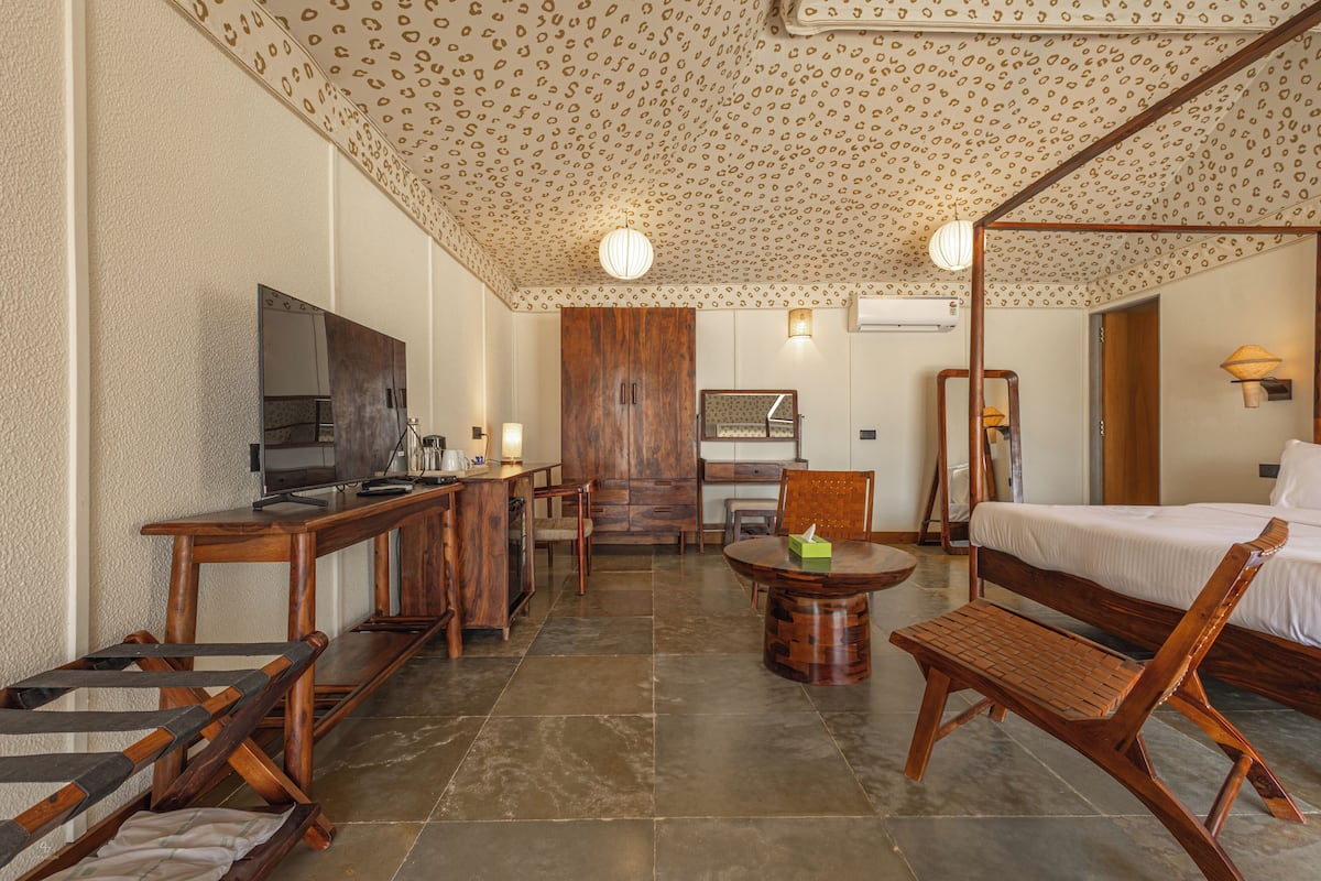 A hotel room with a wooden bed, a TV, a desk, and a dining area with chairs and a table.