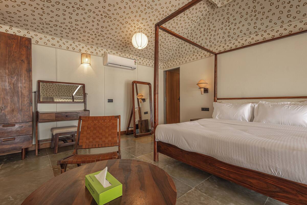 A bedroom with a four-poster bed, a wooden desk with a chair, a small table with a tissue box, and a mirror on the wall.