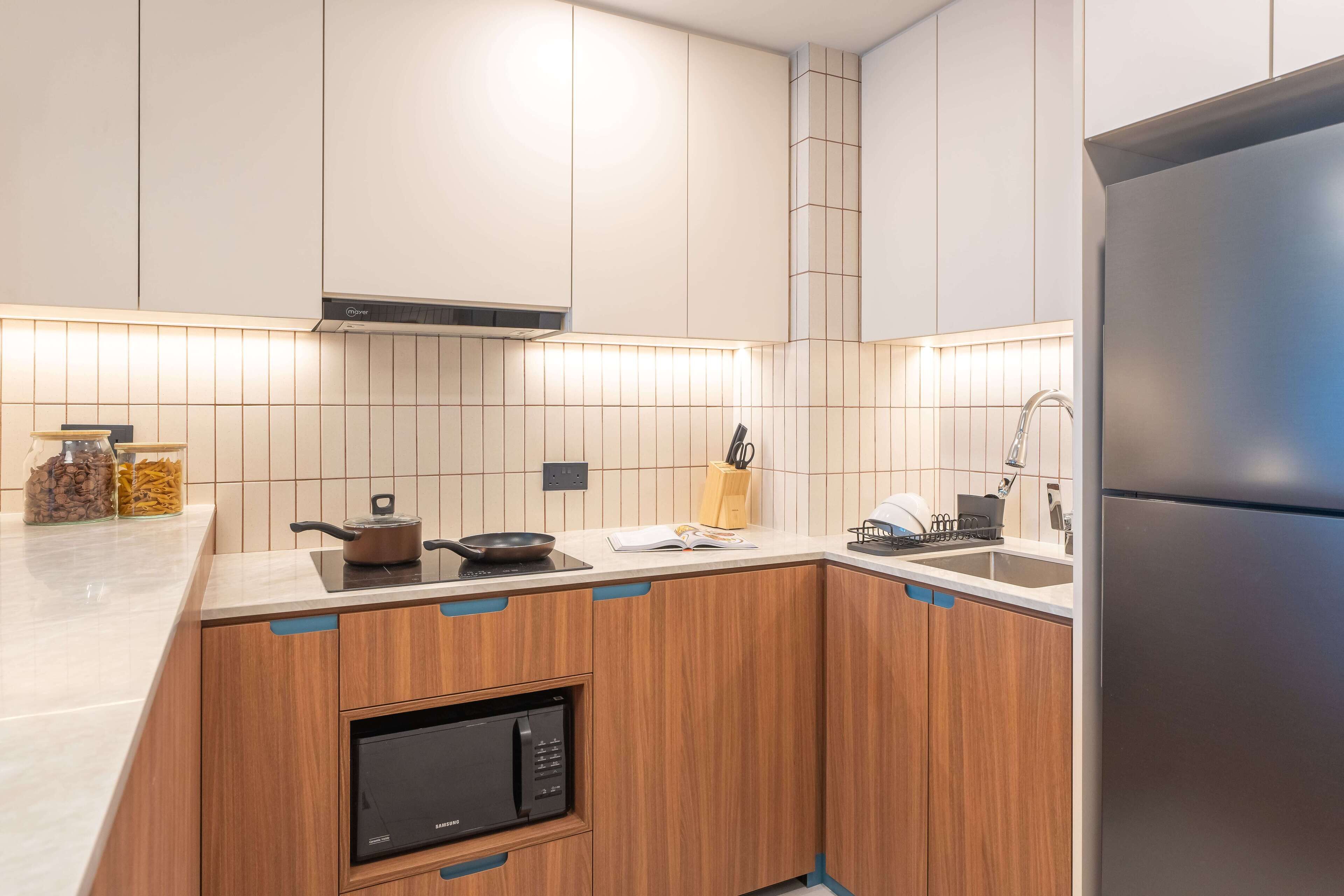 A modern kitchen with wooden cabinets, a built-in microwave, and a stainless steel refrigerator.