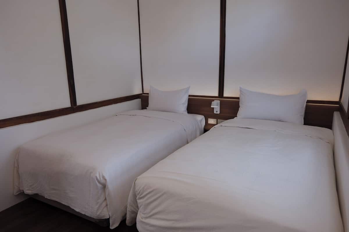 A hotel room with two single beds, wooden headboards, and a white wall.