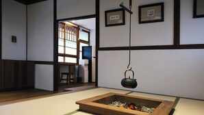 Una habitación con esteras de tatami, un hogar japonés tradicional, vigas de madera y un televisor al fondo.