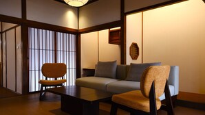 Una habitación de estilo japonés tradicional con suelo de tatami, una mesa de madera baja, un sofá y una silla.