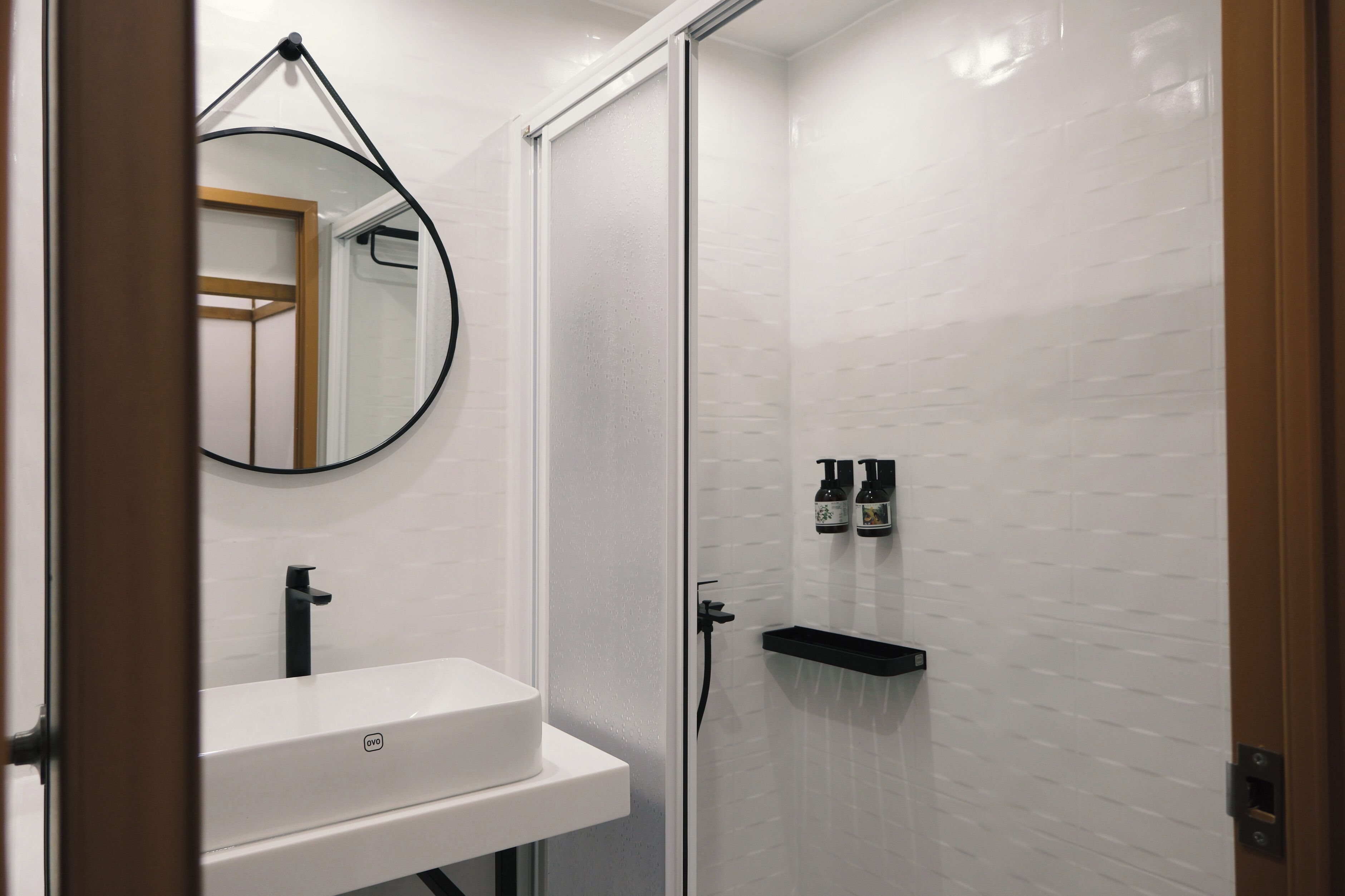 A bathroom with a white sink, a round mirror, and a shower area with a glass door.