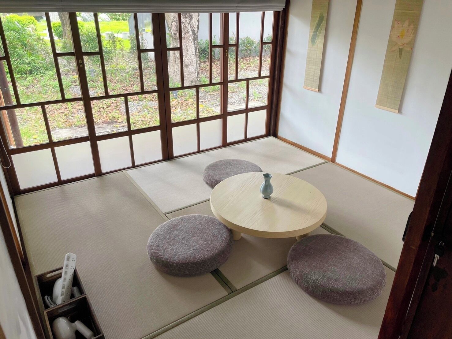 Una habitación japonesa tradicional con suelo de tatami, una mesa baja con un florero y cojines.
