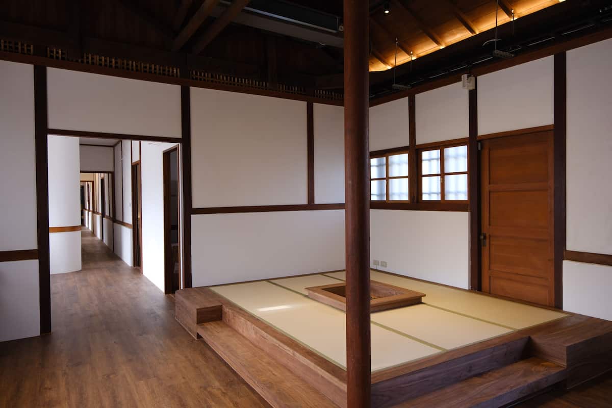 A traditional Japanese room with tatami flooring, a low wooden bed, sliding doors, and a corridor leading to another room.