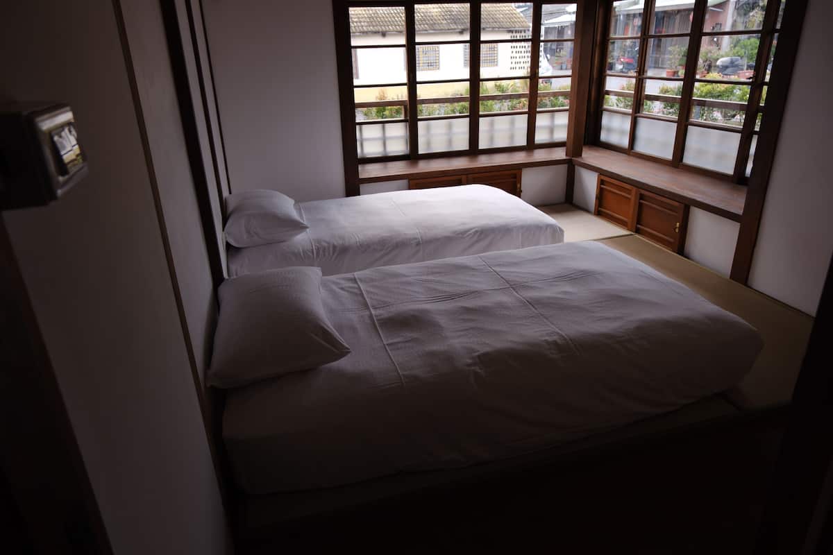 A room with two beds, a wooden bench, and a view through large windows.