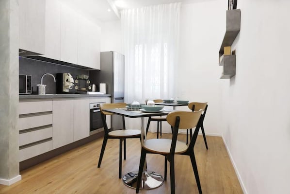A modern kitchen with white cabinetry, a dining area with a table and chairs, and a window with sheer curtains.