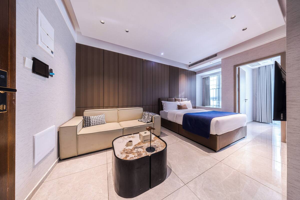 A modern hotel room with a bed, a sofa, a coffee table, and a TV.