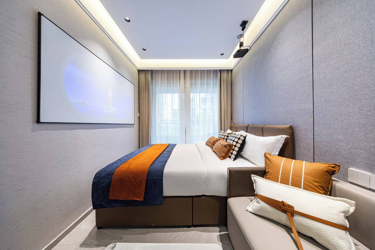 A modern hotel room with a large bed, a sofa, a flat-screen TV, and a ceiling light fixture.