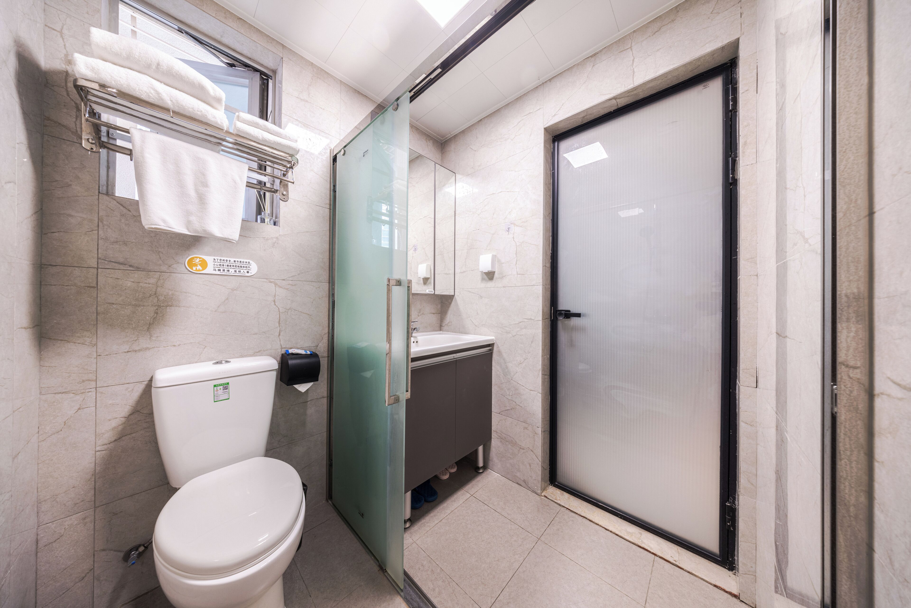 Ein Badezimmer mit Toilette, Waschbecken, einer Duschkabine aus Glas und einem Handtuchhalter mit gefalteten Handtüchern.