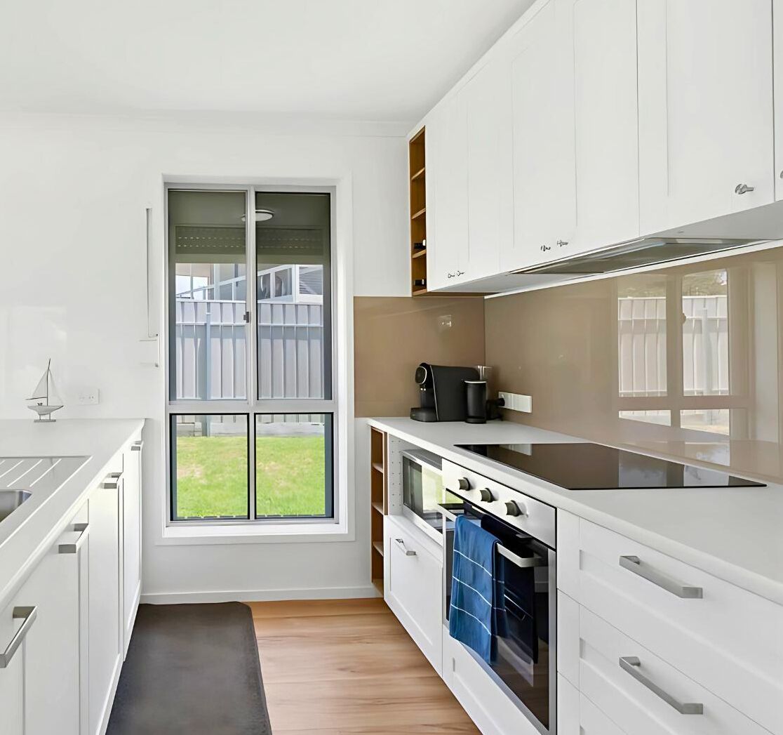 Una cucina moderna con mobili bianchi, un'ampia finestra e vista sul giardino.