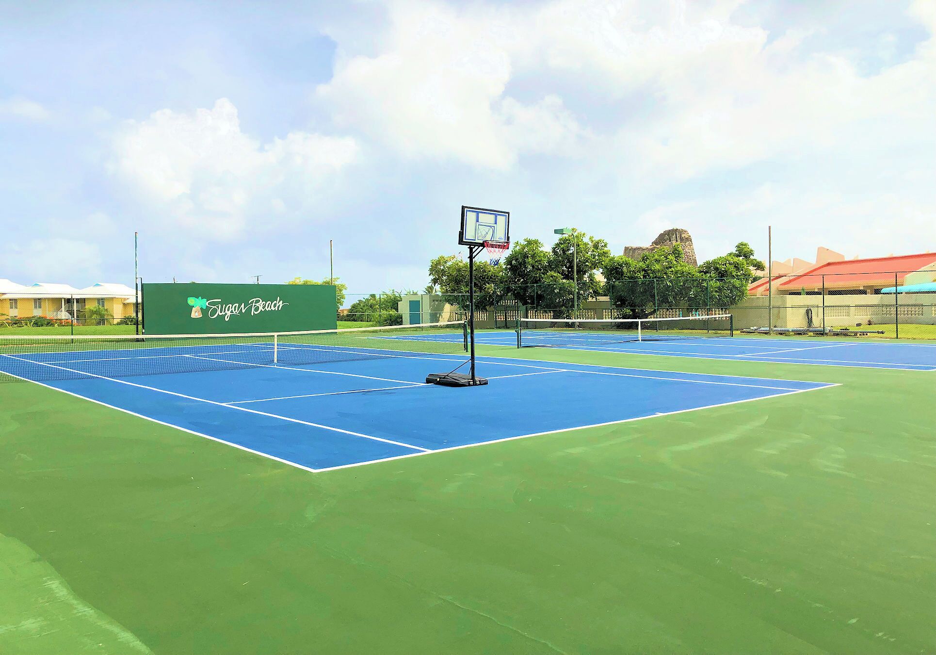 Una cancha de tenis con una red, un aro de baloncesto y un cartel que dice 'Sugar Beach'.