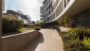 A curved building with balconies, a paved walkway, and landscaped areas with shrubs and trees. - GuestHost - Ostiense Modern & Stylish Apt with Terrace (Roma)