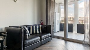 A modern living room with a black leather sofa, a small table, and a sliding glass door leading to an outdoor balcony. - GuestHost - Ostiense Modern & Stylish Apt with Terrace (Roma)