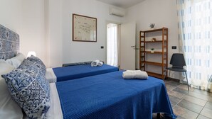 Ein Hotelzimmer mit zwei Betten, einem Holzregal, einem Sessel und einer Deckenleuchte.
