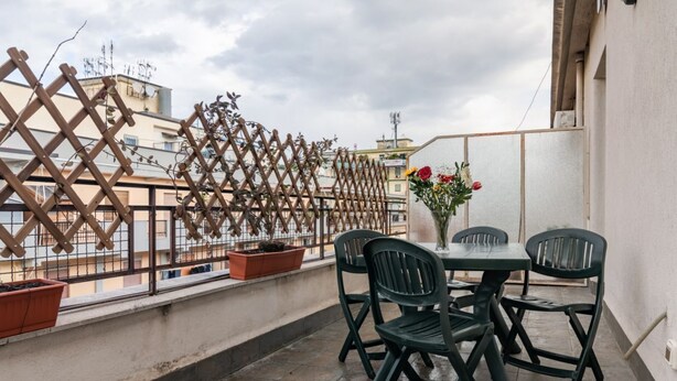 Ein Balkon mit Tisch und Stühlen, Blumentöpfen und Blick auf Gebäude.