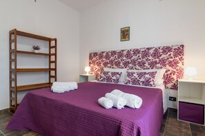 Une chambre d’hôtel avec un lit, une étagère en bois, une tête de lit ornée d’un motif floral et un petit tableau accroché au mur.