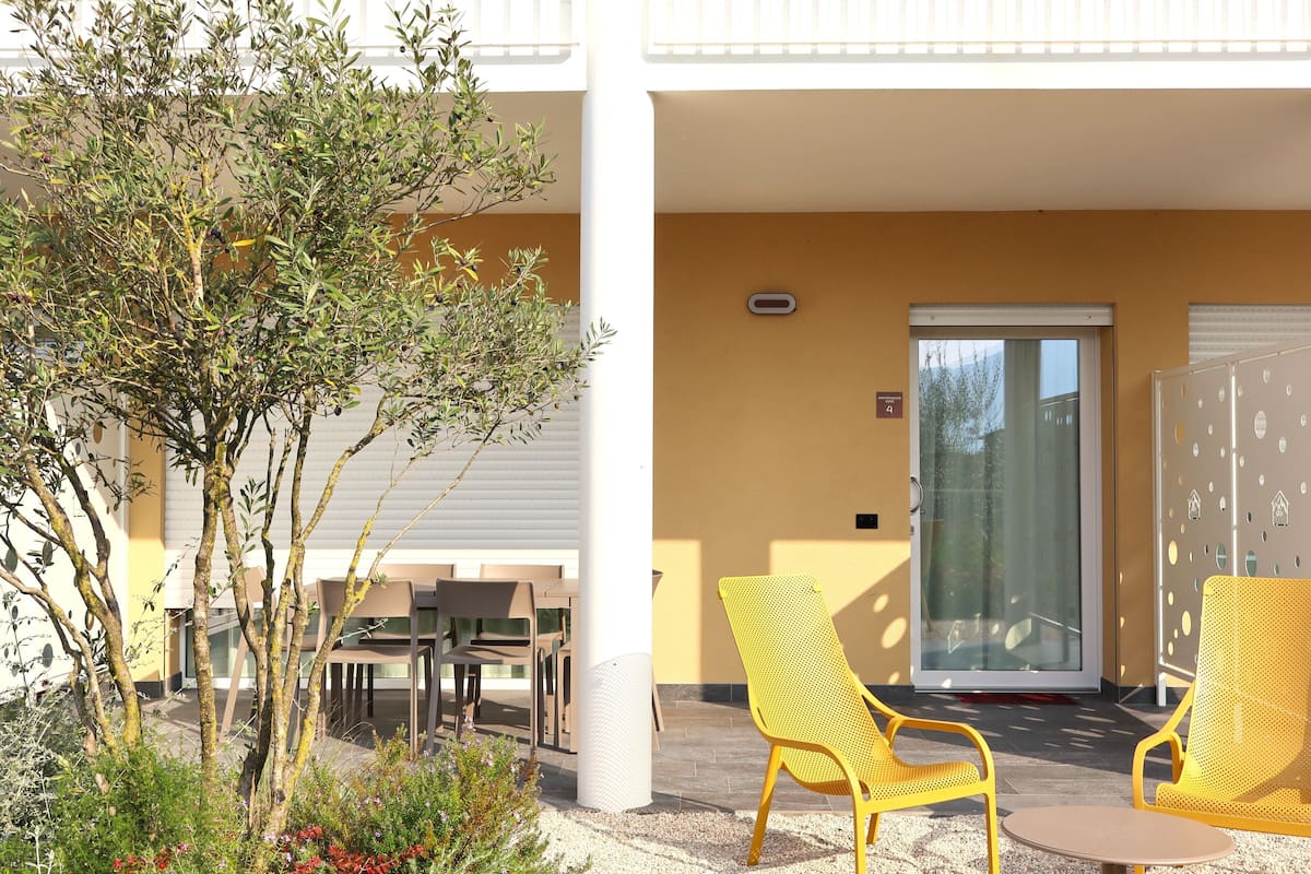 Uma área de estar externa com cadeiras amarelas, uma mesa e uma porta que dá para o interior.