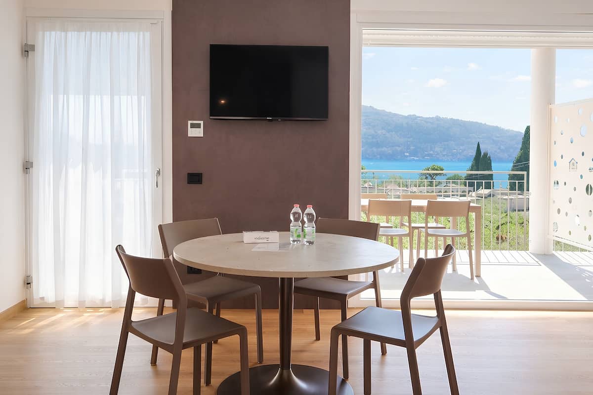 Uma sala de jantar moderna com uma mesa redonda, cadeiras, uma TV de tela plana na parede e vista para o mar e montanhas através de grandes janelas.