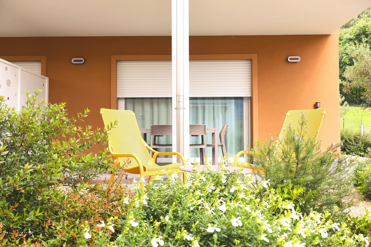 Uma varanda com cadeiras amarelas, uma mesa e vista para o jardim.