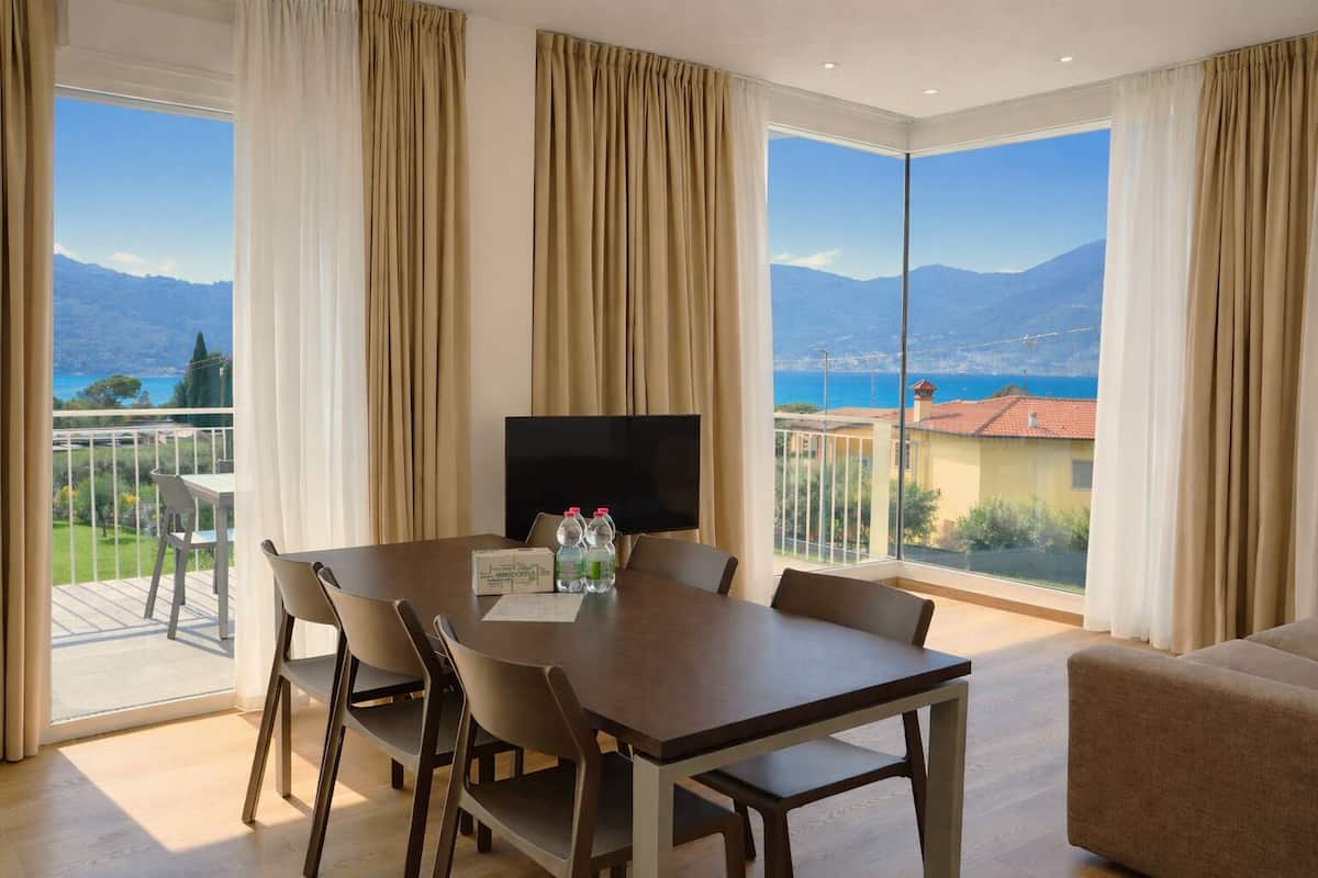 Quarto de hotel com varanda, uma mesa de jantar, cadeiras, televisão e sofá.