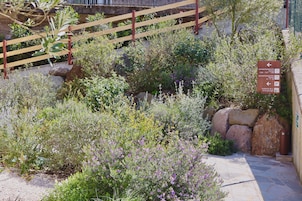 Un jardín con cerca de madera, un sendero de piedra y un cartel que indica la dirección a los apartamentos y al garaje.