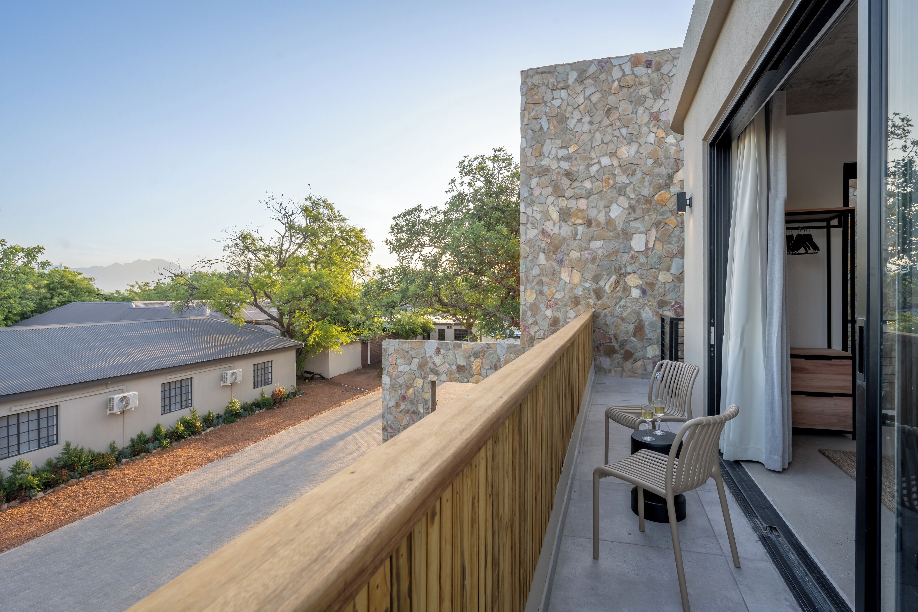 A balcony with a stone wall, a wooden railing, and a seating area with chairs and a table.