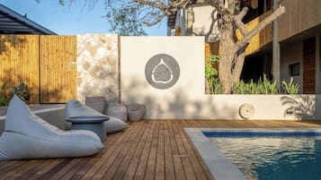 A wooden deck with a pool, stone wall, and a tree.