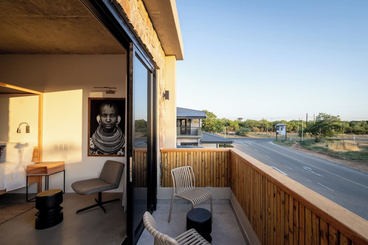 Un balcon avec une balustrade en bois, un lit avec une tête de lit en bois, une chaise et une petite table ronde.