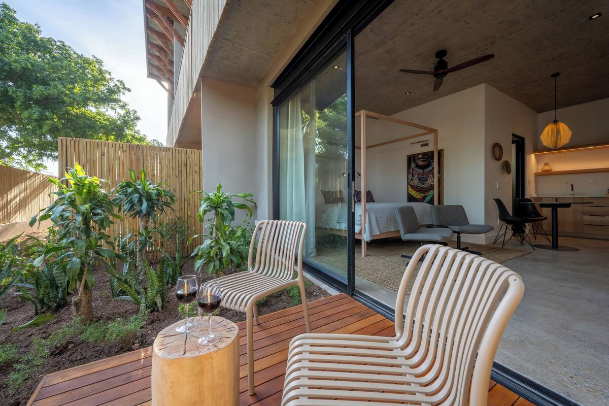Une terrasse extérieure moderne avec un plancher en bois, deux fauteuils en osier et une petite table sur laquelle se trouve un verre à vin.
