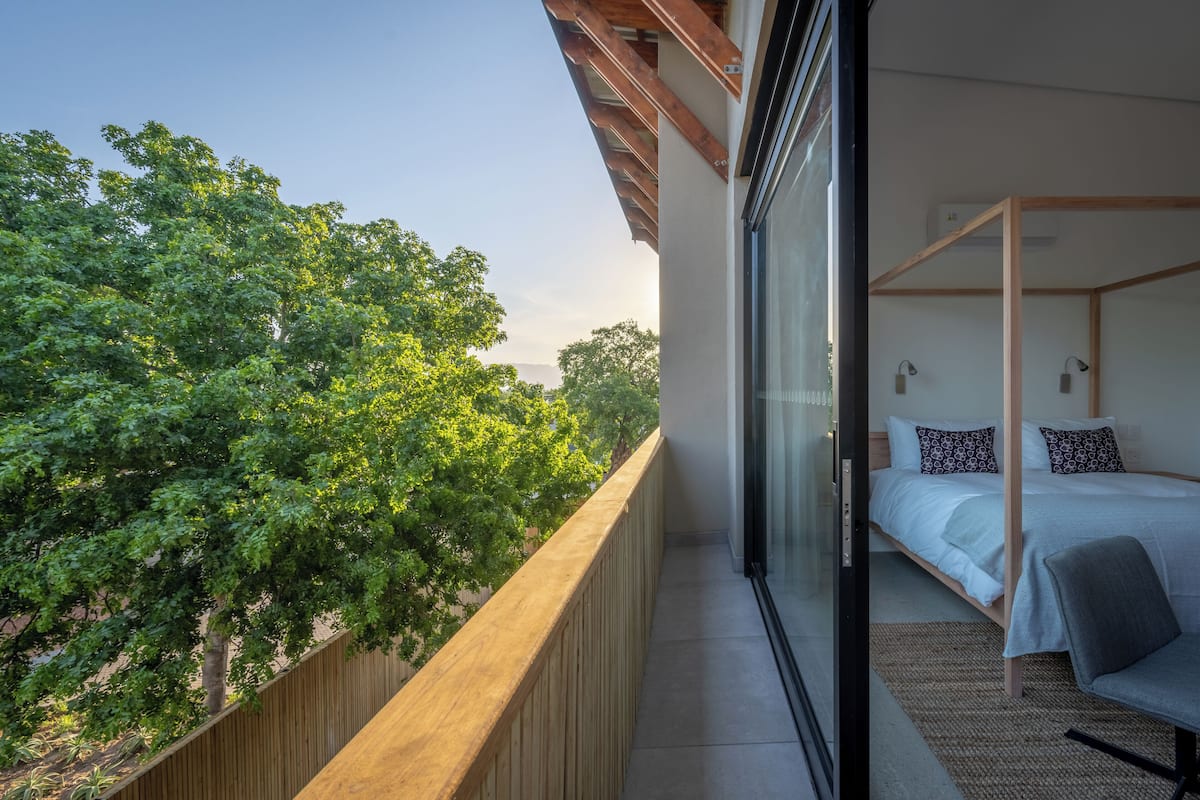 Un balcon avec une balustrade en bois, un lit à baldaquin et une vue sur les arbres.