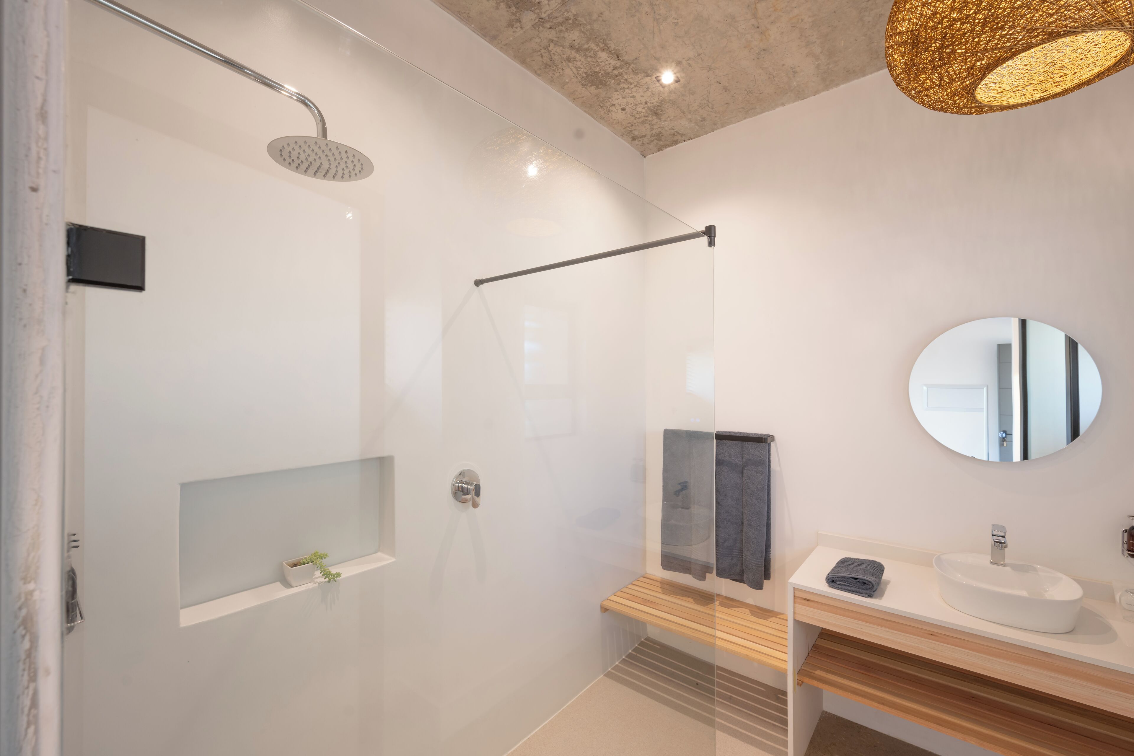 A modern bathroom with a glass-enclosed shower, a wooden vanity, a round mirror, and a ceiling light fixture.