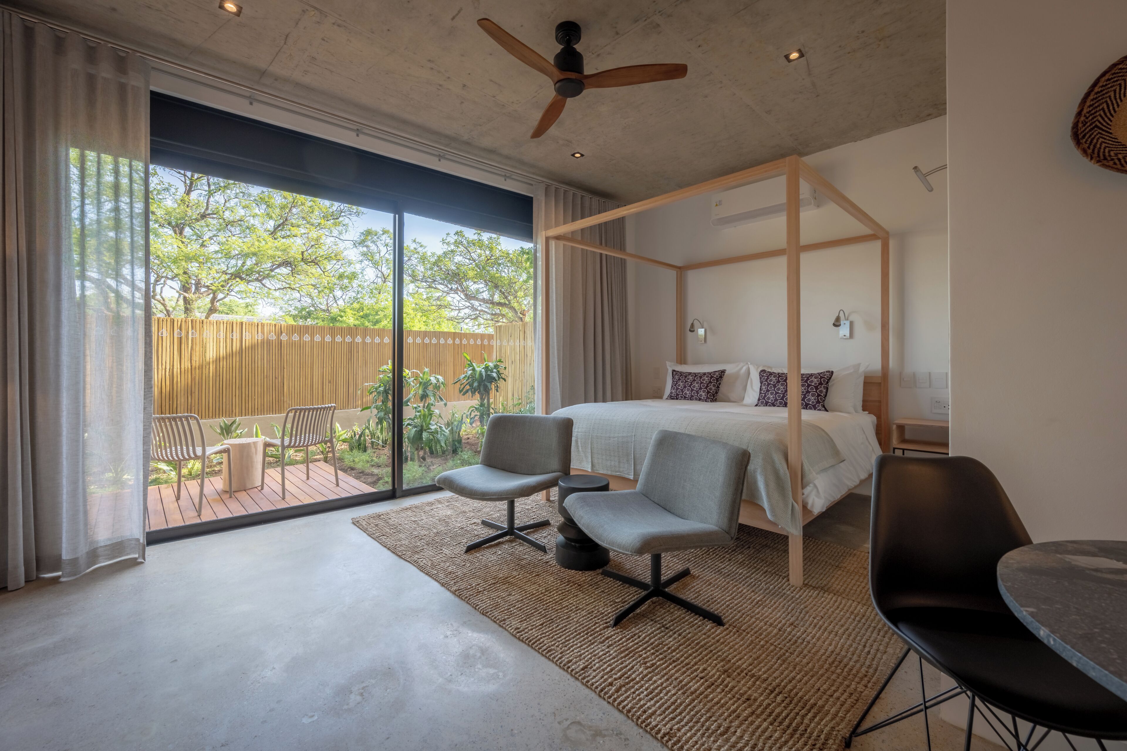 A modern bedroom with a four-poster bed, a ceiling fan, and a view of the outdoors.
