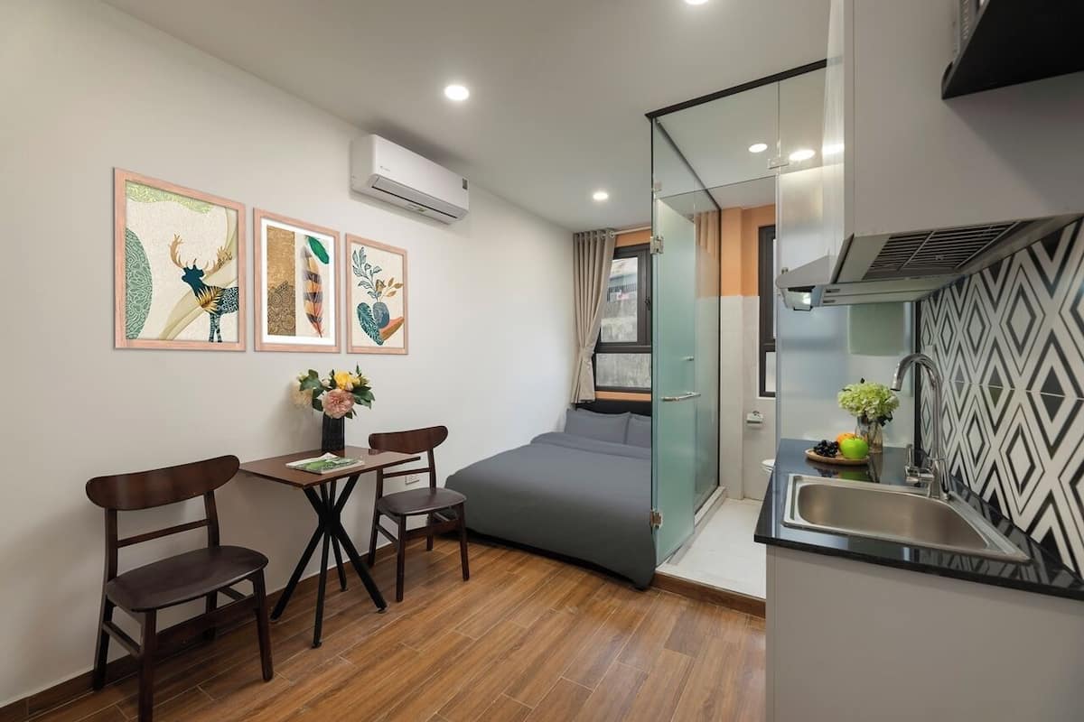Een compacte kamer met een bed, een klein tafeltje met stoelen, een kitchenette en drie ingelijste kunstwerken aan de wand.