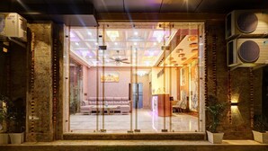 A hotel entrance with a glass door, air conditioning units, a green mat, and a reception desk.