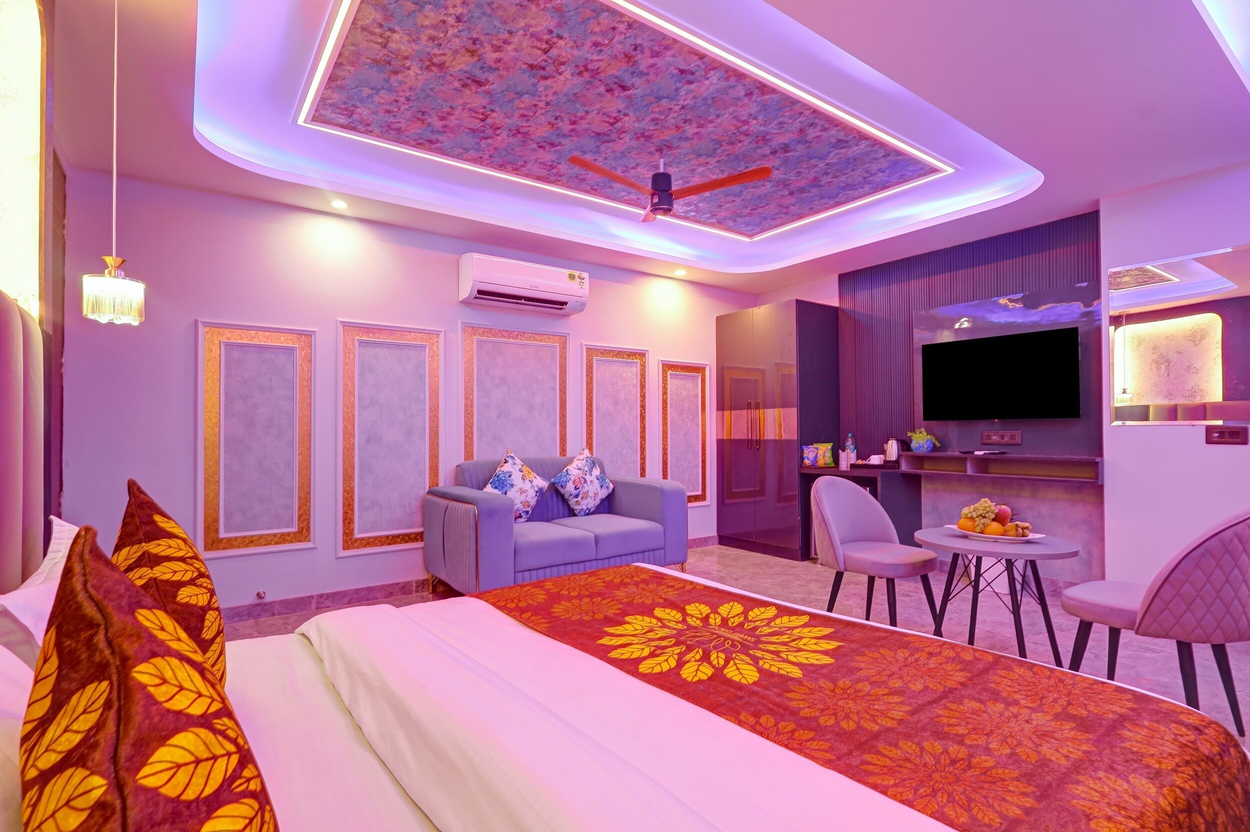 A modern hotel room with a large bed, a sofa, a dining area, and a TV.