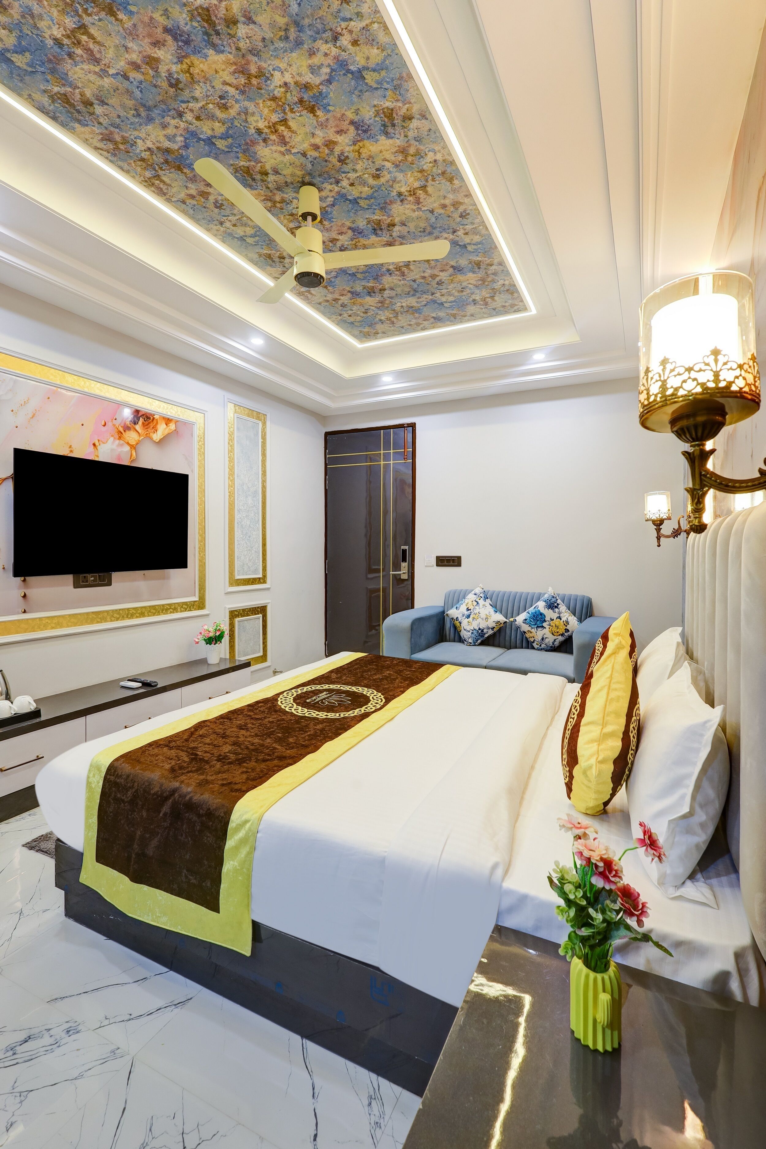 Une chambre d’hôtel moderne dotée d’un grand lit, d’un téléviseur à écran plat, d’un ventilateur de plafond et d’un lustre.