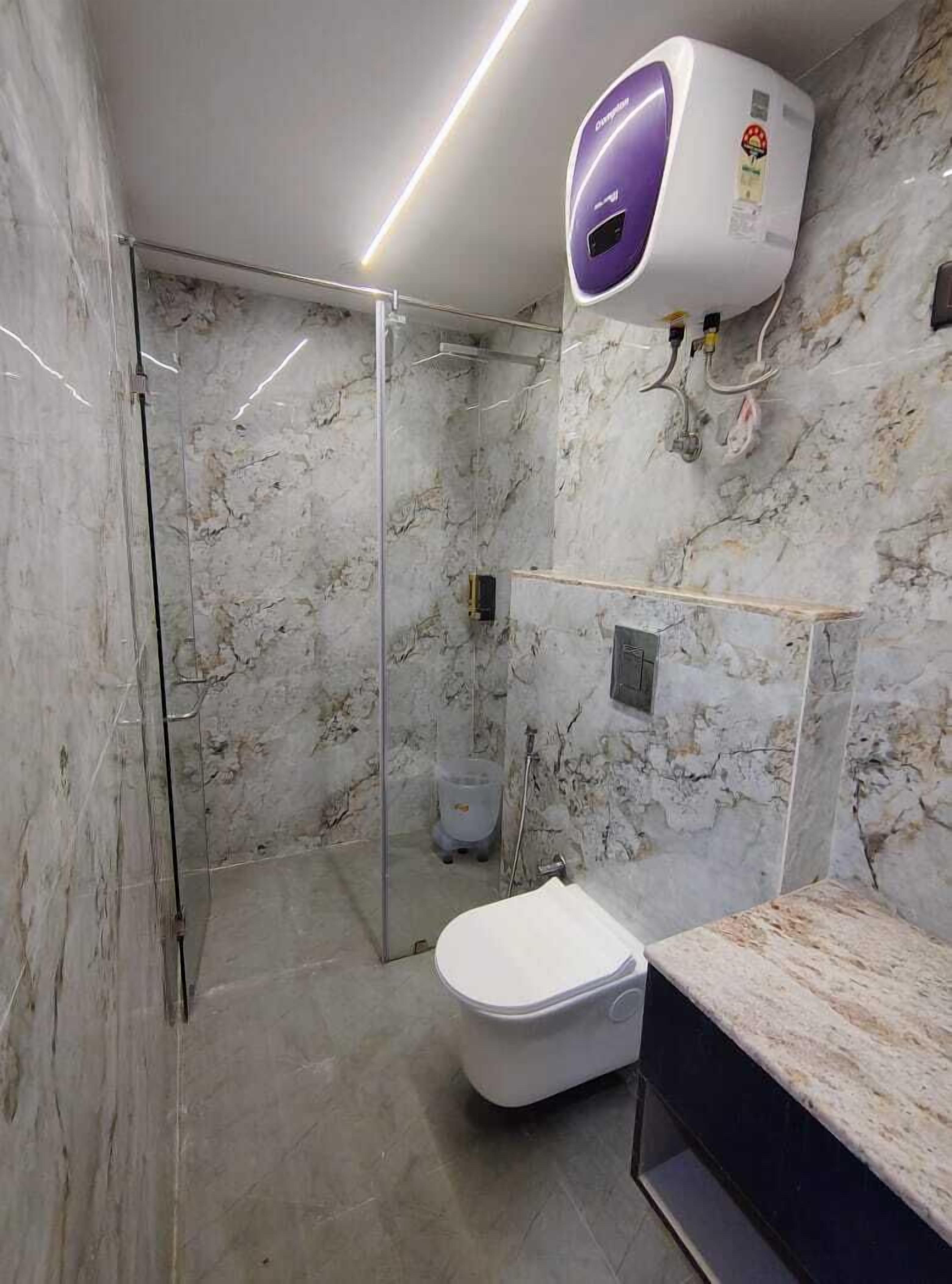 A modern bathroom with a marble wall, a glass shower enclosure, a toilet, and a built-in sink.
