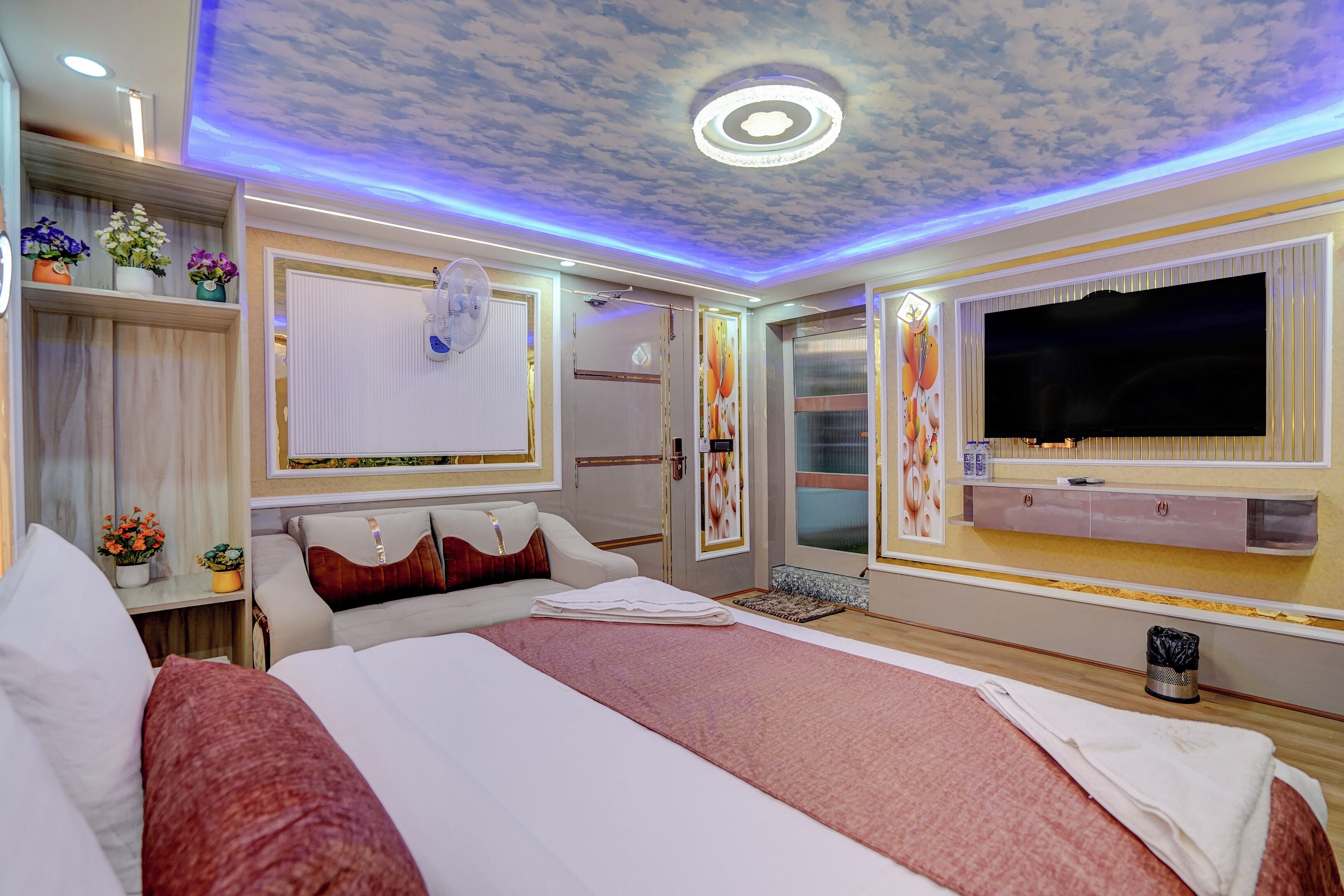 Une chambre d’hôtel dotée d’un grand lit, d’un téléviseur à écran plat, d’un plafond décoré de motifs nuageux et d’une étagère murale agrémentée d’objets décoratifs.