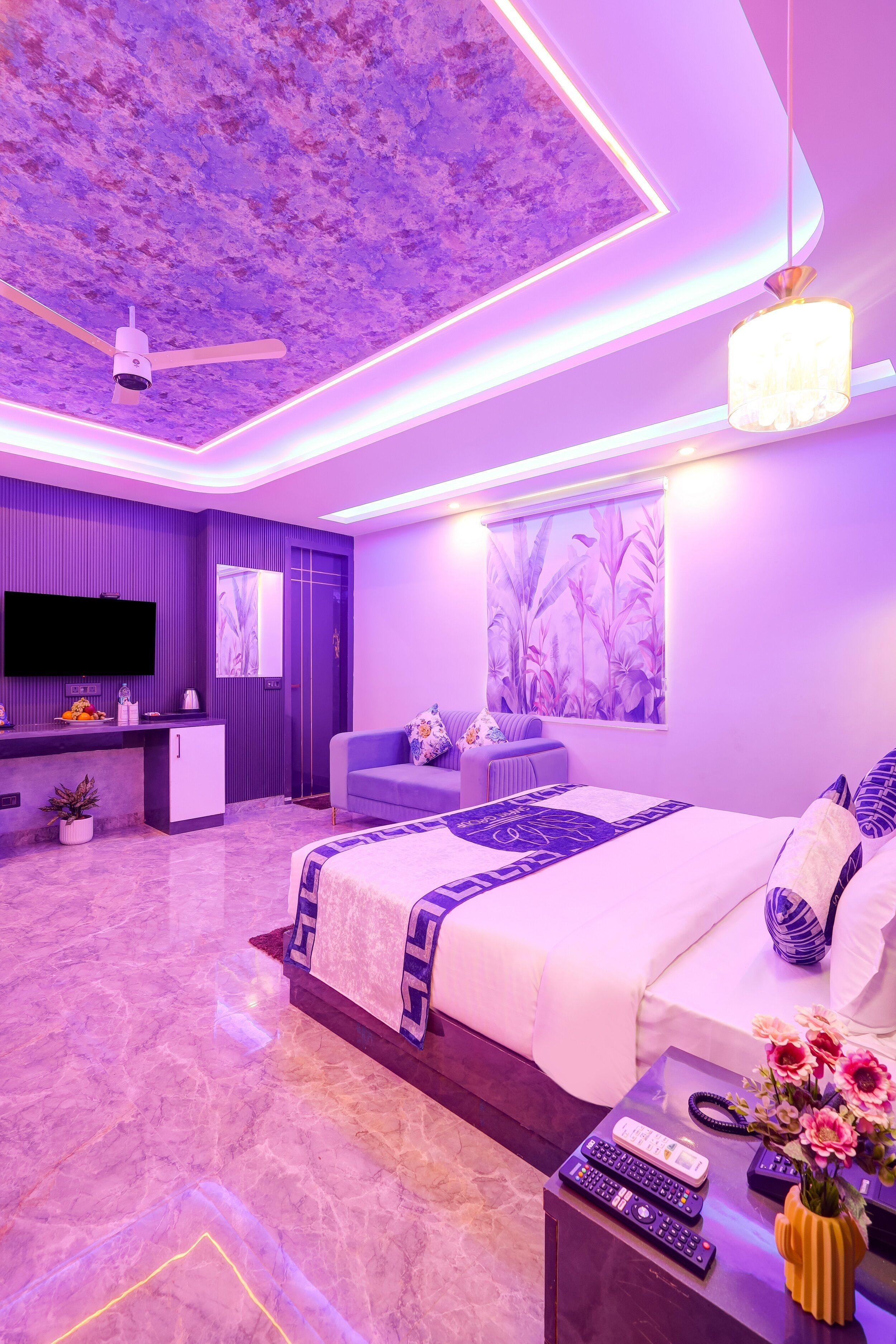 Een moderne slaapkamer met een groot bed, een televisie, een zithoek en een plafondventilator.