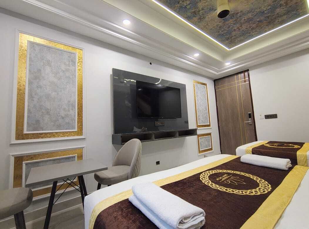 A hotel room with a flat-screen TV mounted on the wall, a desk with a chair, and two beds with towels.
