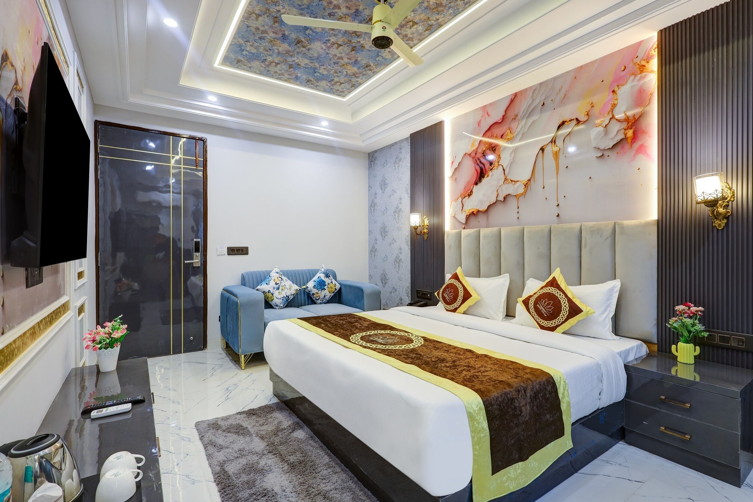 A modern bedroom with a large bed, a television, a sofa, and a decorative wall.