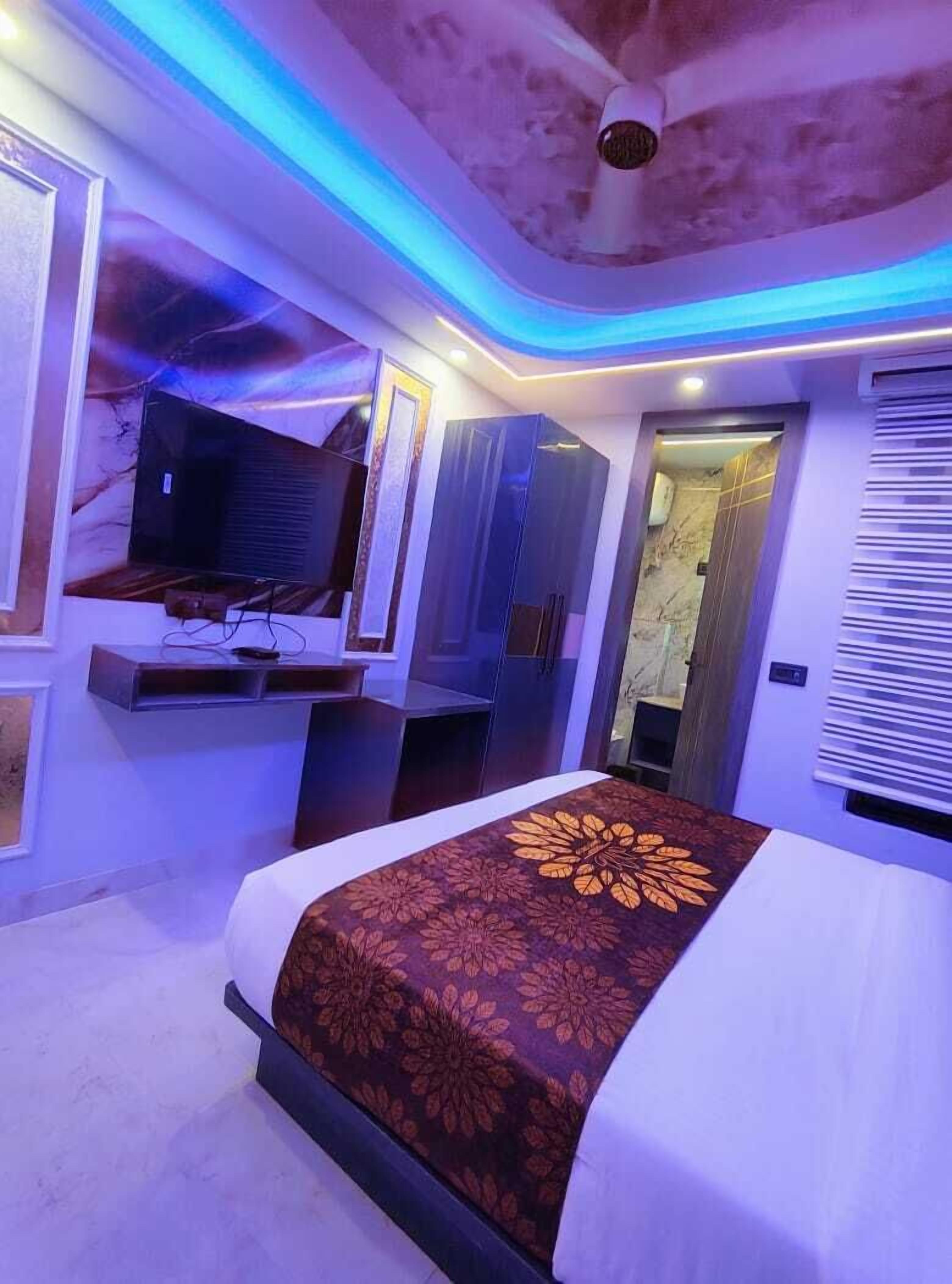 A modern hotel room with a bed, a flat-screen TV, a vanity with a mirror, and a ceiling fan.