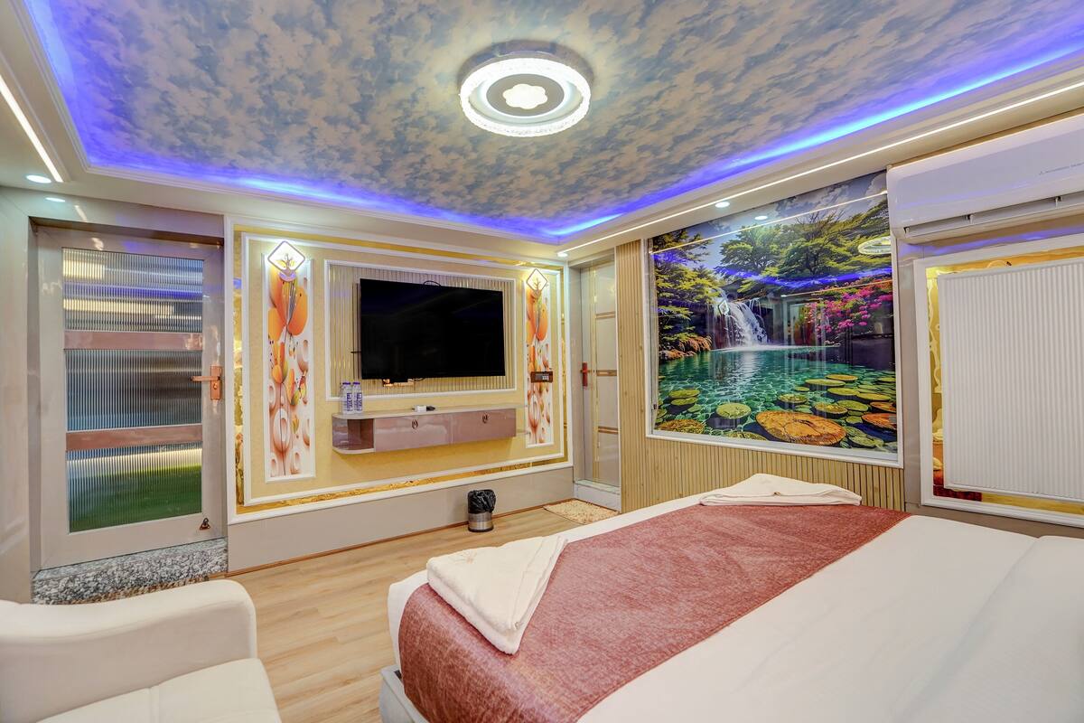 Hotelkamer met een bed, een televisie, een wanddecoratie van een waterval en een plafond met een wolkpatroon.