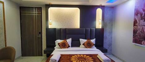 Una habitación de hotel moderna con una cama grande, cabecera oscura e iluminación empotrada en el techo.